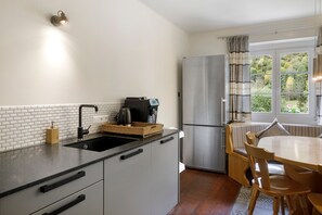 Una cocina compacta con un lavamanos negro, una cafetera, un refrigerador de acero inoxidable y una zona de comedor con mesa y sillas.