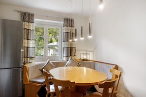 A dining area with a round wooden table, cushioned bench seating, and a stainless steel refrigerator.