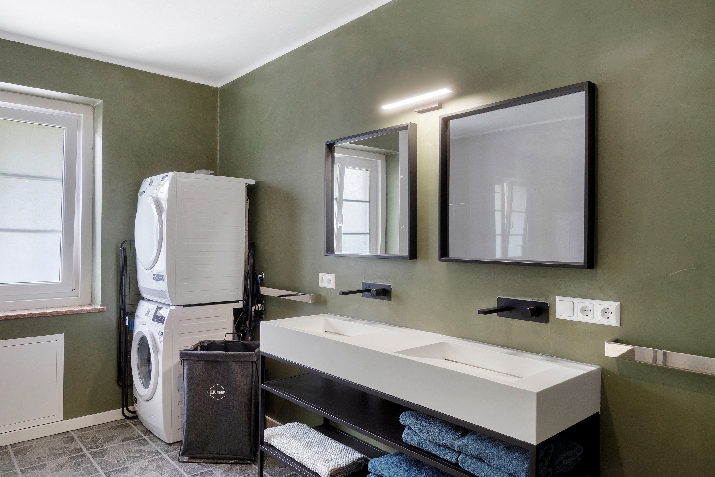 Een moderne badkamer met een ingebouwde wasmachine, een grote spiegel en een witte wastafel.