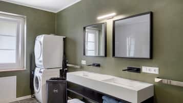 Een moderne badkamer met een ingebouwde wasmachine, een grote spiegel en een witte wastafel.