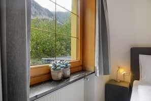 Habitación de hotel con vista a una zona boscosa, una mesita de noche con lámpara y un radiador.