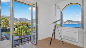 Ein Zimmer mit einer großen Schiebetür, die auf einen Balkon mit Blick auf Berge und Meer führt.