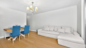 Ein modernes Wohnzimmer mit Essbereich, einem weißen Sofa, blauen Stühlen und einer Kristallleuchter.