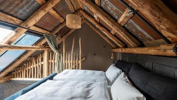 Ein Zimmer mit hohen Decken und geneigtem Dach, ein Bett mit weißer Bettwäsche, eine Hängeleuchte und ein Fenster.