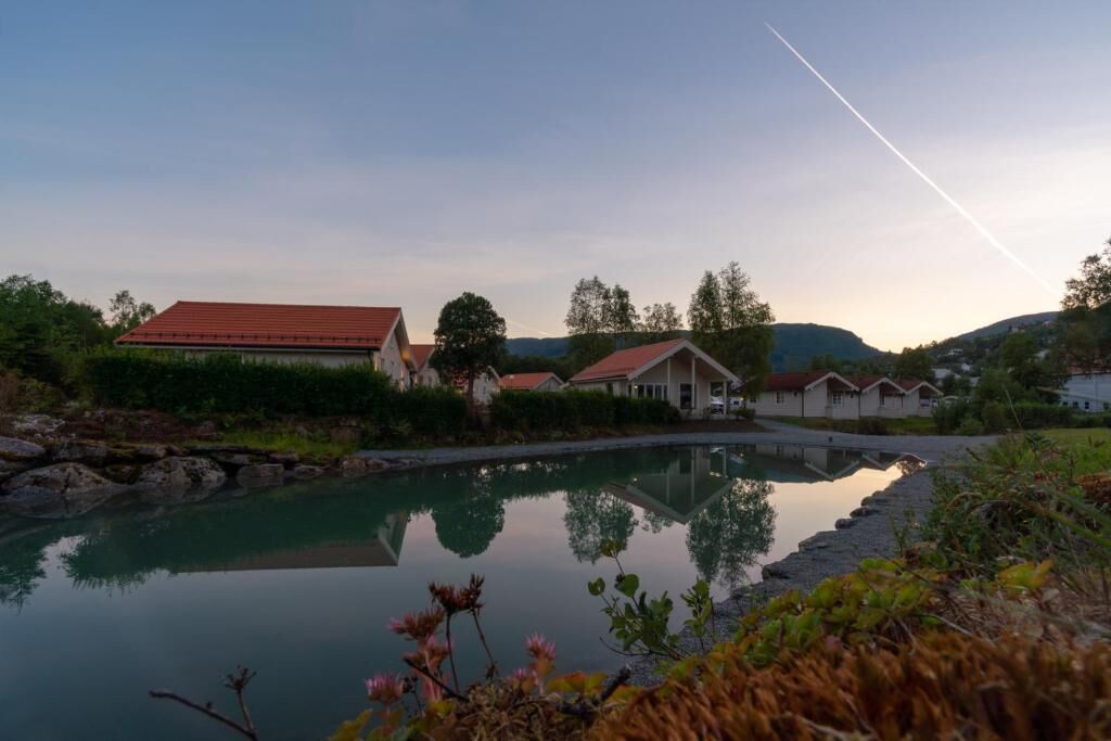 A serene lakeside setting with a row of houses, a clear sky, and a visible contrail.