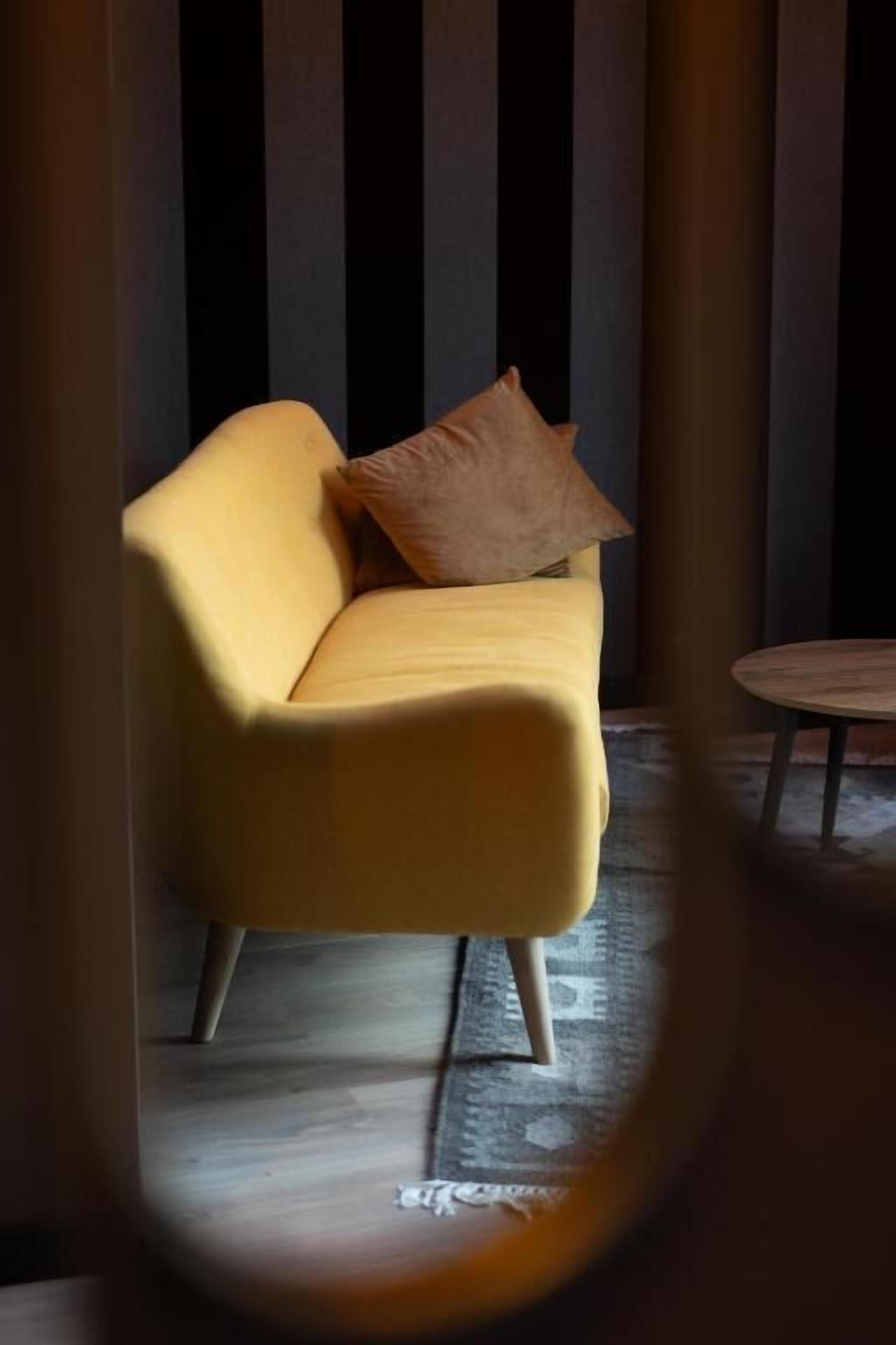 A yellow sofa with a brown pillow in a room with striped wallpaper and a patterned rug.