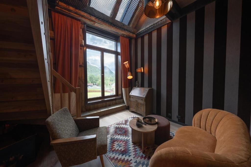 Ein Zimmer mit Holzeinrichtung, einem Fenster mit Vorhängen, einem kleinen Tisch und einem Sofa.