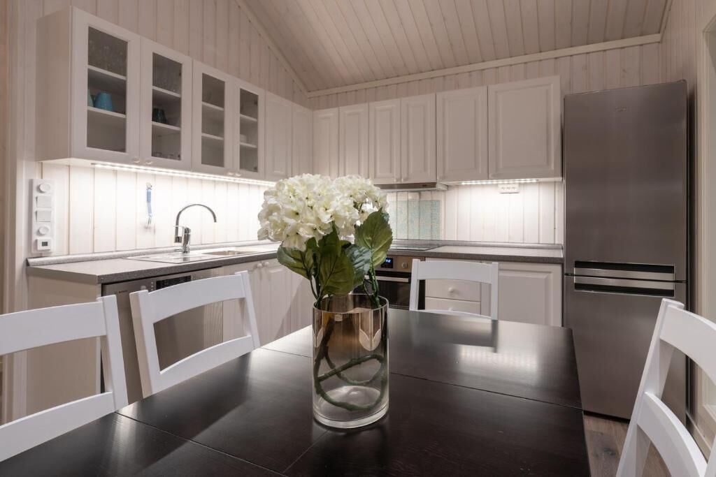 Une cuisine moderne avec des meubles blancs, un réfrigérateur en acier inoxydable et un vase rempli de fleurs blanches placé sur la table.