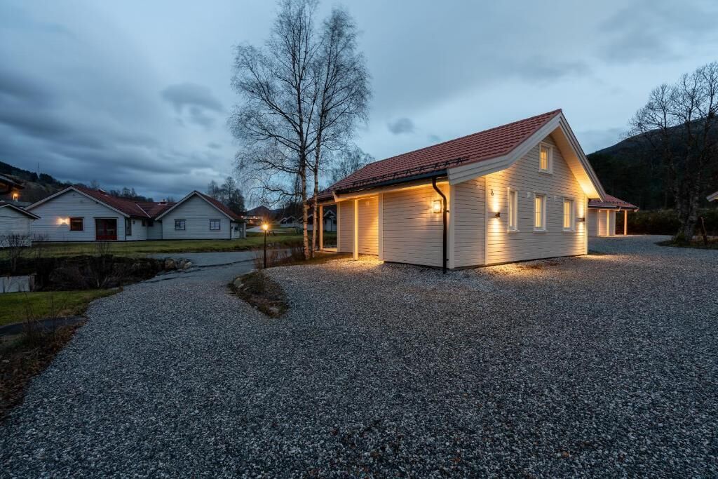 A house with a gravel driveway, a red roof, and a lighted exterior.