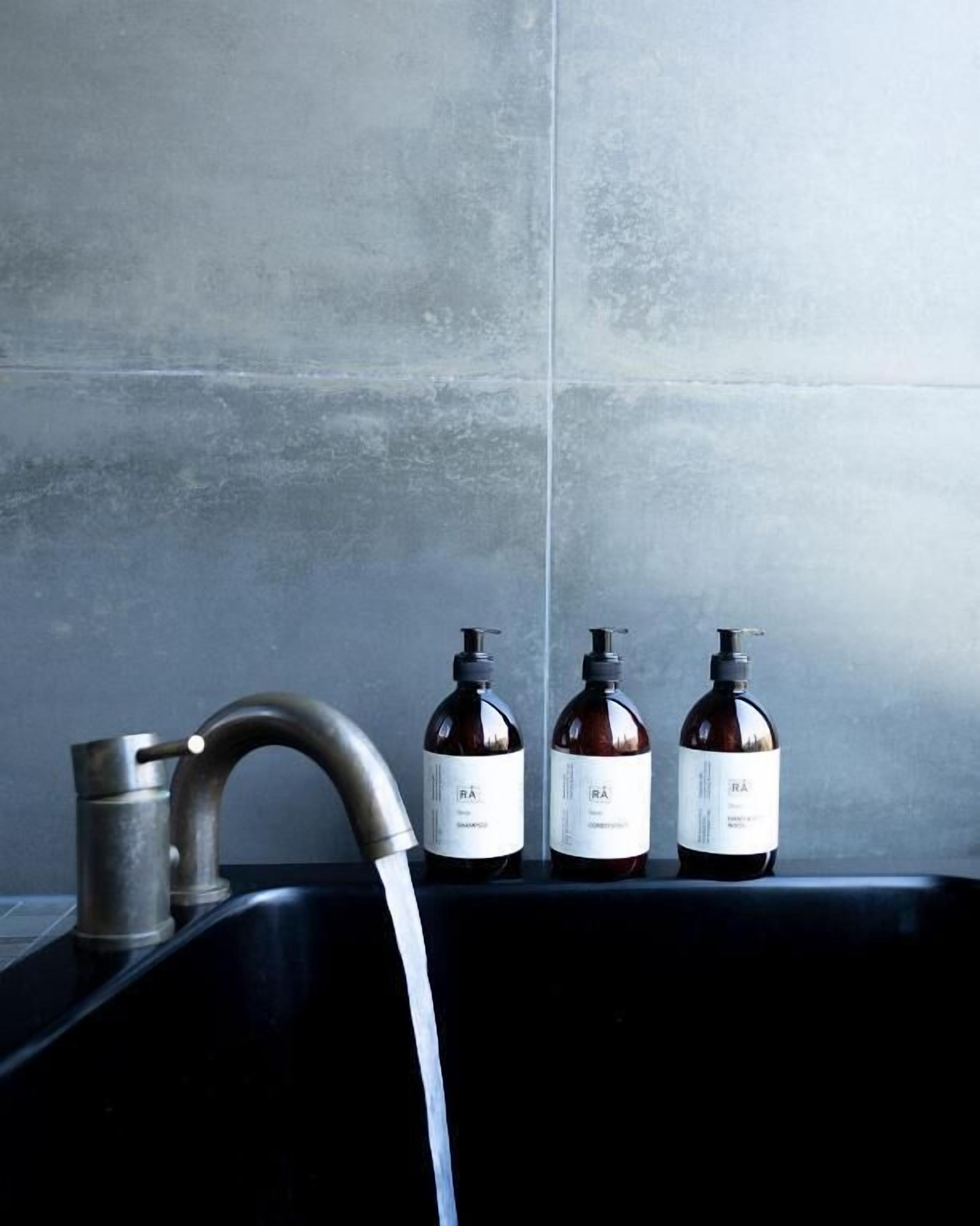 A bathroom with a black sink, a faucet, and three bottles of liquid soap on the edge.