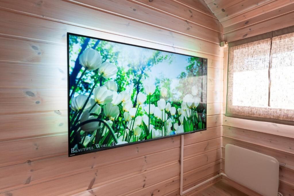 Un televisor montado en una pared de madera en una habitación con ventana y radiador.