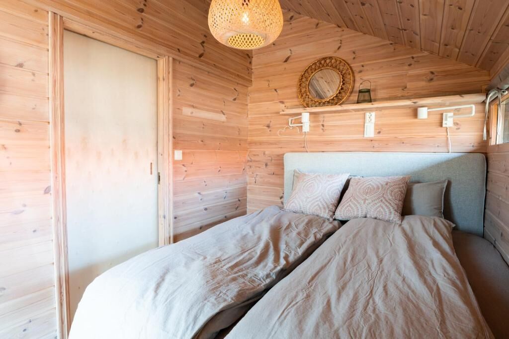 Un dormitorio de cabaña de madera con una cama, una lámpara colgante y un estante en la pared.