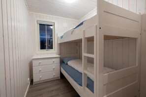 A bunk bed room with a window, a desk with drawers, and a wooden floor.