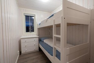 Habitación con literas, un escritorio con cajones y piso de madera.