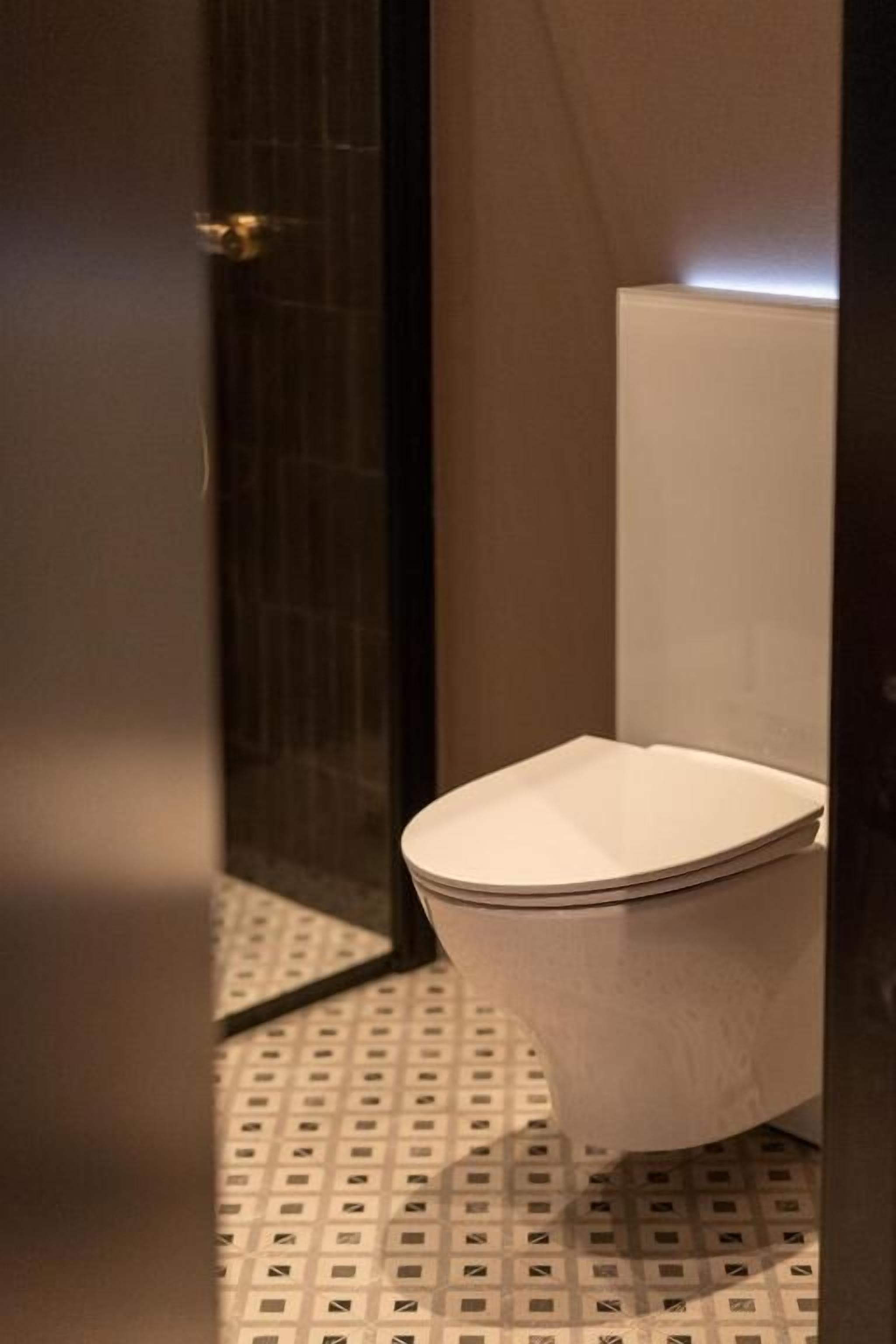 A bathroom with a toilet, a patterned floor, and a dark wall.