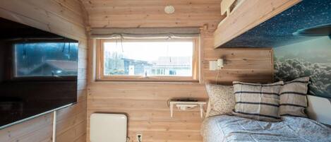 Interior de una cabaña de madera con una cama, una mesita, una ventana y un mural en el techo.