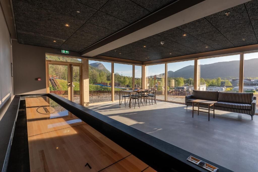 Un espacio interior amplio con mesa de billar, zona de estar con sofá y sillones, y grandes ventanales con vistas a un paisaje montañoso.