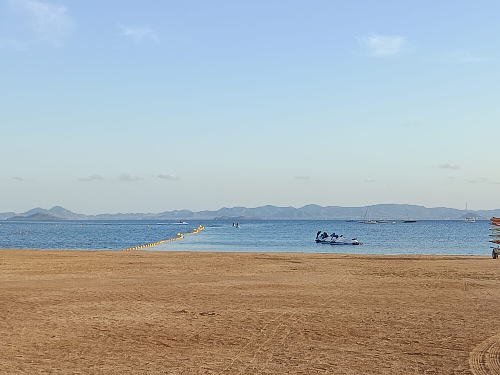 Een strand met een heldere lucht, kalme zee en verre bergen.