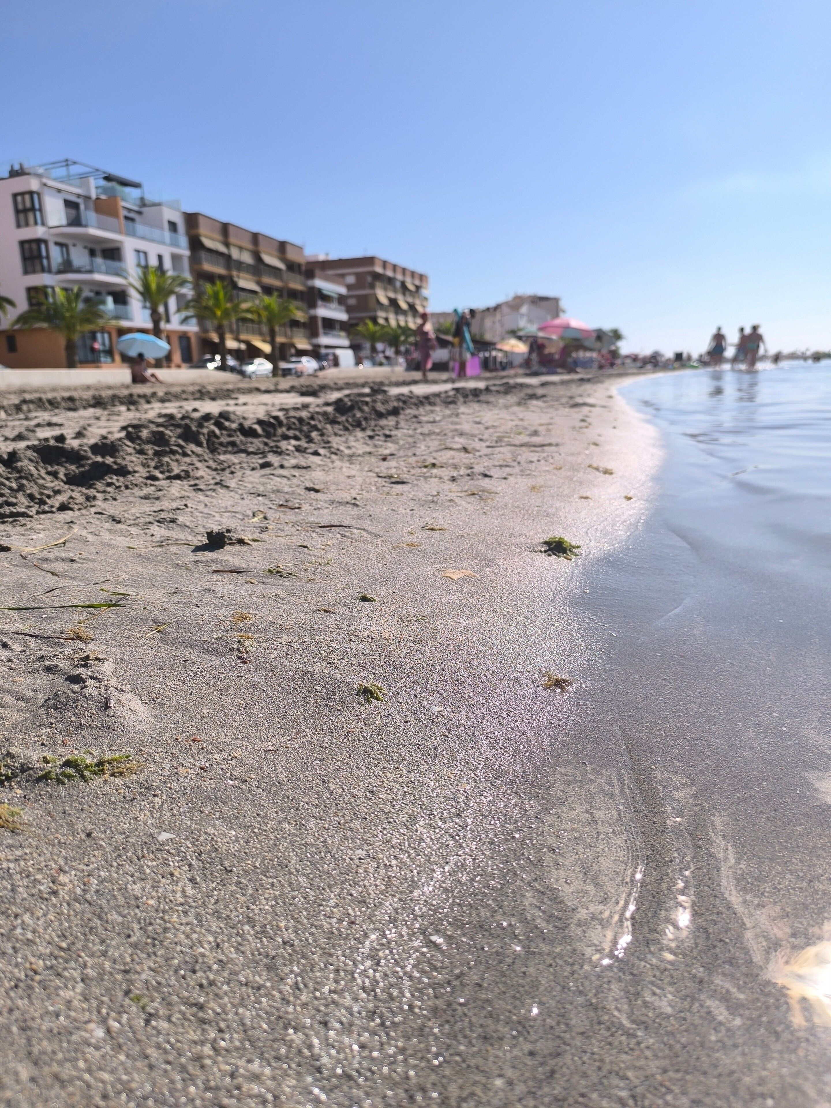 Une plage avec un rivage sablonneux, des bâtiments en arrière-plan et un ciel dégagé.
