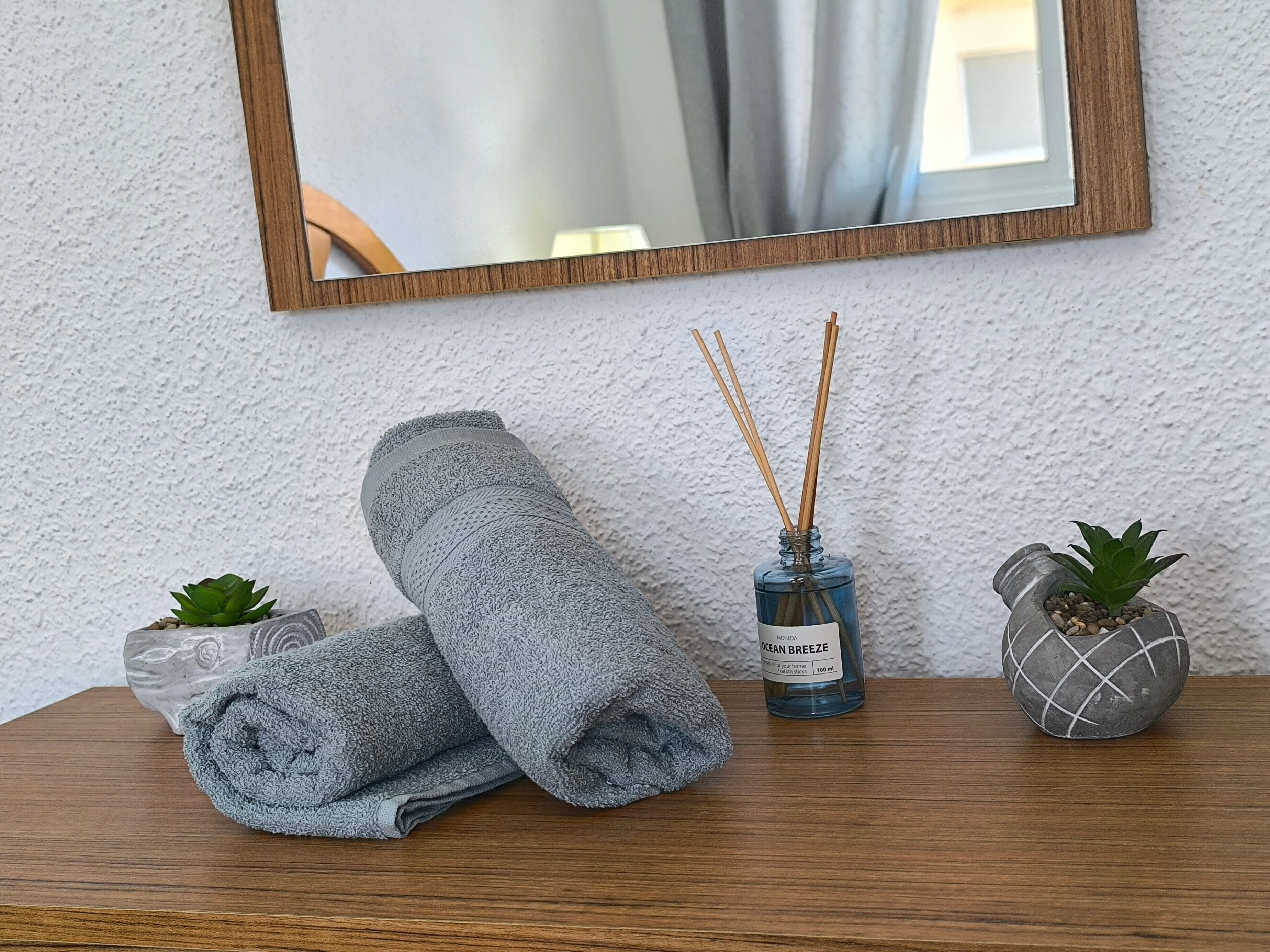 A wooden table with a rolled towel, a blue bottle labeled 'OCEAN BREEZE,' reed diffusers, and a small potted plant.