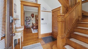 A wooden staircase leading to a second floor, a welcome sign, a door with a basket, and a hallway with a rug. - Illini Dream House with Historic Retreat near UIUC and Downtown (Champaign)