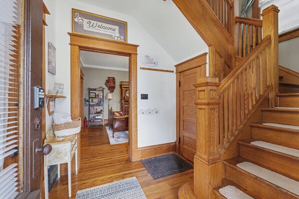 A wooden staircase leading to a second floor, a welcome sign, a door with a basket, and a hallway with a rug.