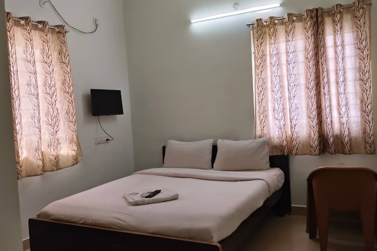 Un dormitorio con cama, una silla, un televisor y cortinas.