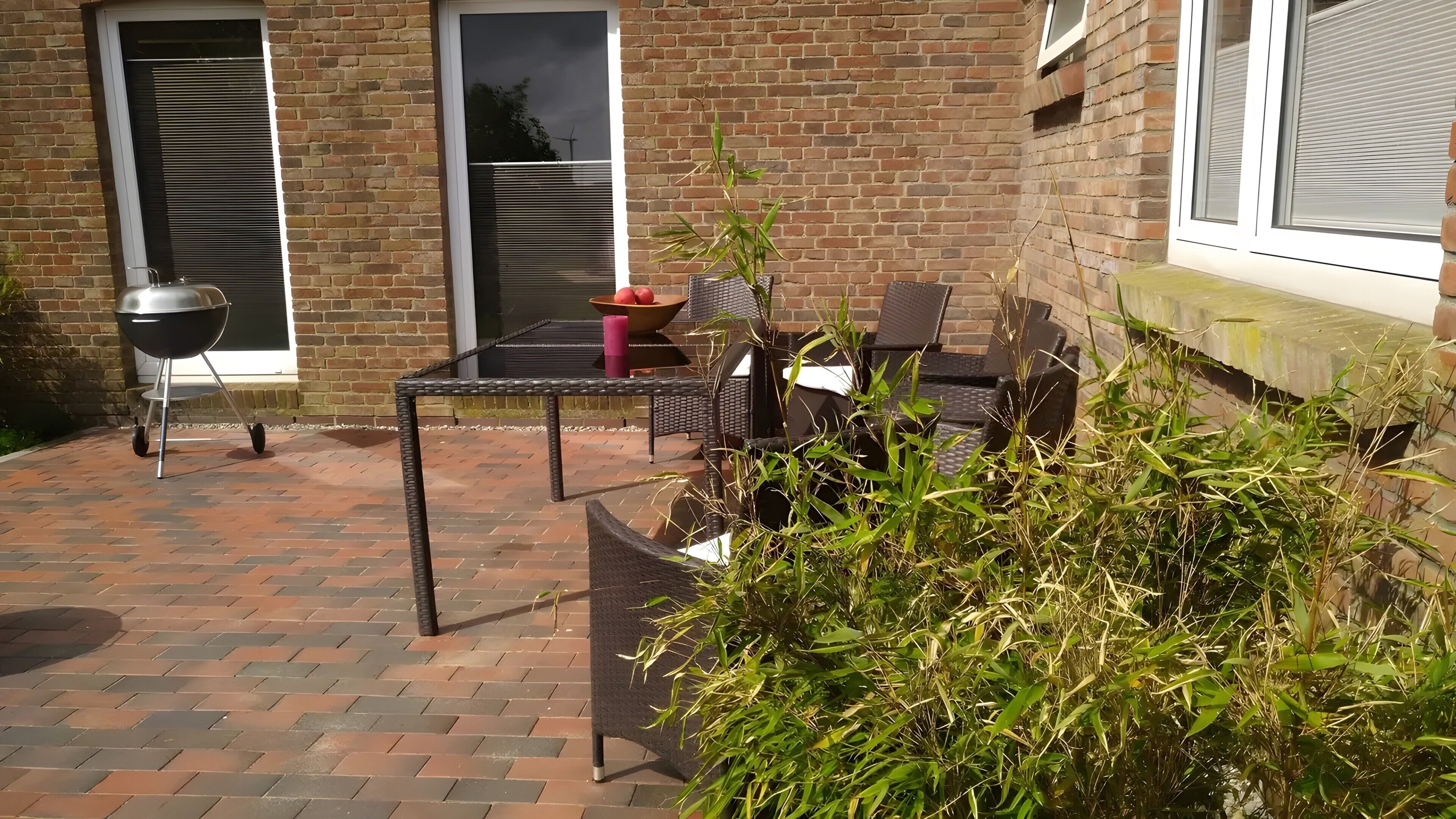 Un patio con piso de ladrillo, una parrilla, mobiliario exterior y una planta en maceta.