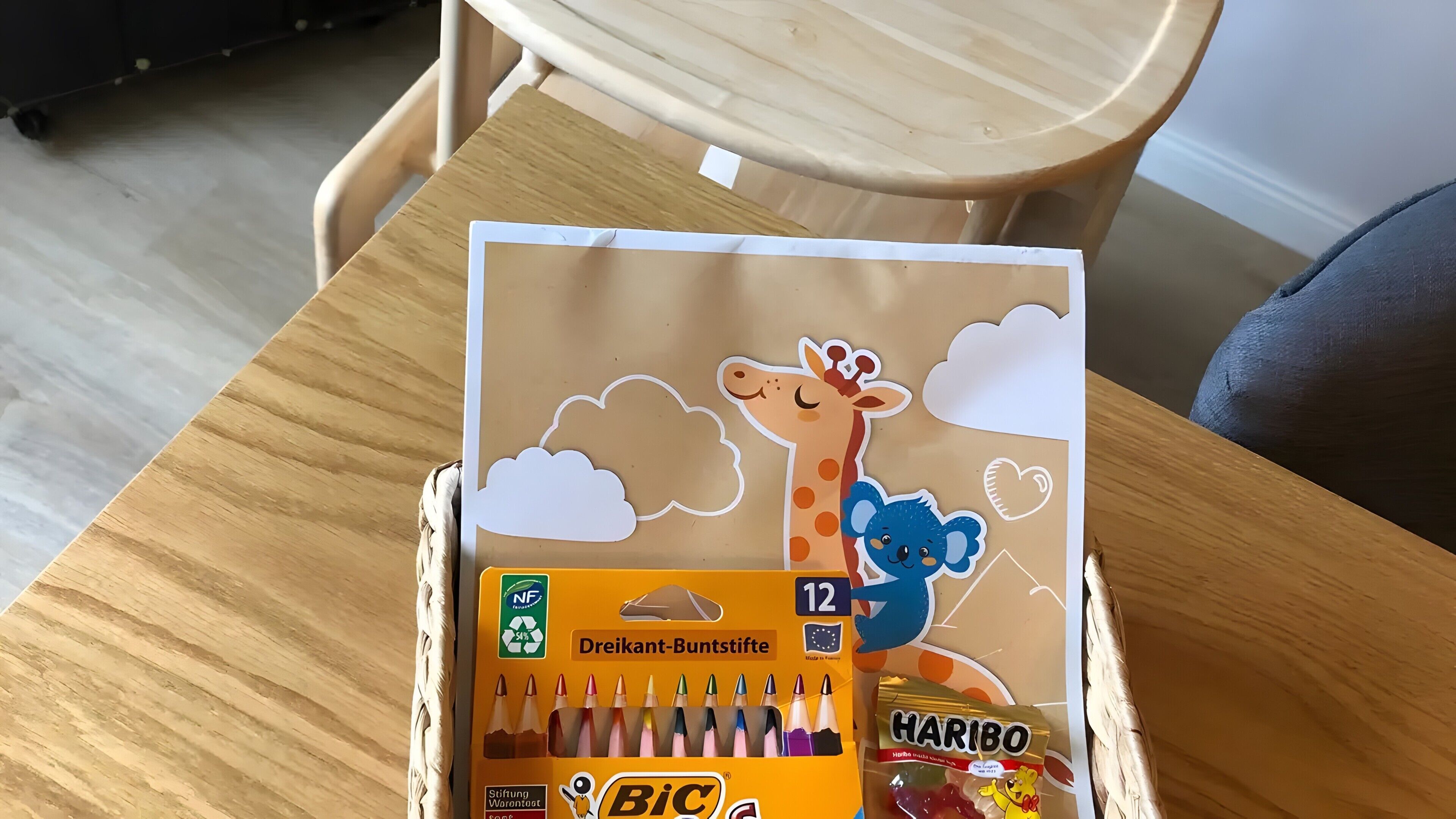 Une boîte contenant du matériel de dessin, notamment des crayons de couleur, une découpe en forme de girafe et d’ours, et un bonbon Haribo.