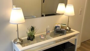 Un comptoir d’accueil d’hôtel avec deux lampes, un miroir, une console avec un plateau en verre, une petite plante et un kit de bienvenue.