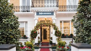Entrada de hotel con alfombra roja, un cartel sobre la puerta y un balcón con barandilla.