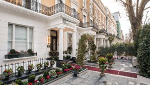 Filas de casas adosadas tradicionales con fachadas blancas, balcones de hierro forjado negro y una alfombra roja que lleva a la entrada.