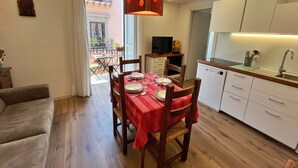 Un espace de vie compact comprenant un coin repas, une kitchenette et donnant sur le balcon extérieur.