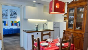 Une cuisine compacte équipée d’un lave-vaisselle, d’une table à manger recouverte de nappes rouges et d’un meuble en bois aux portes vitrées.