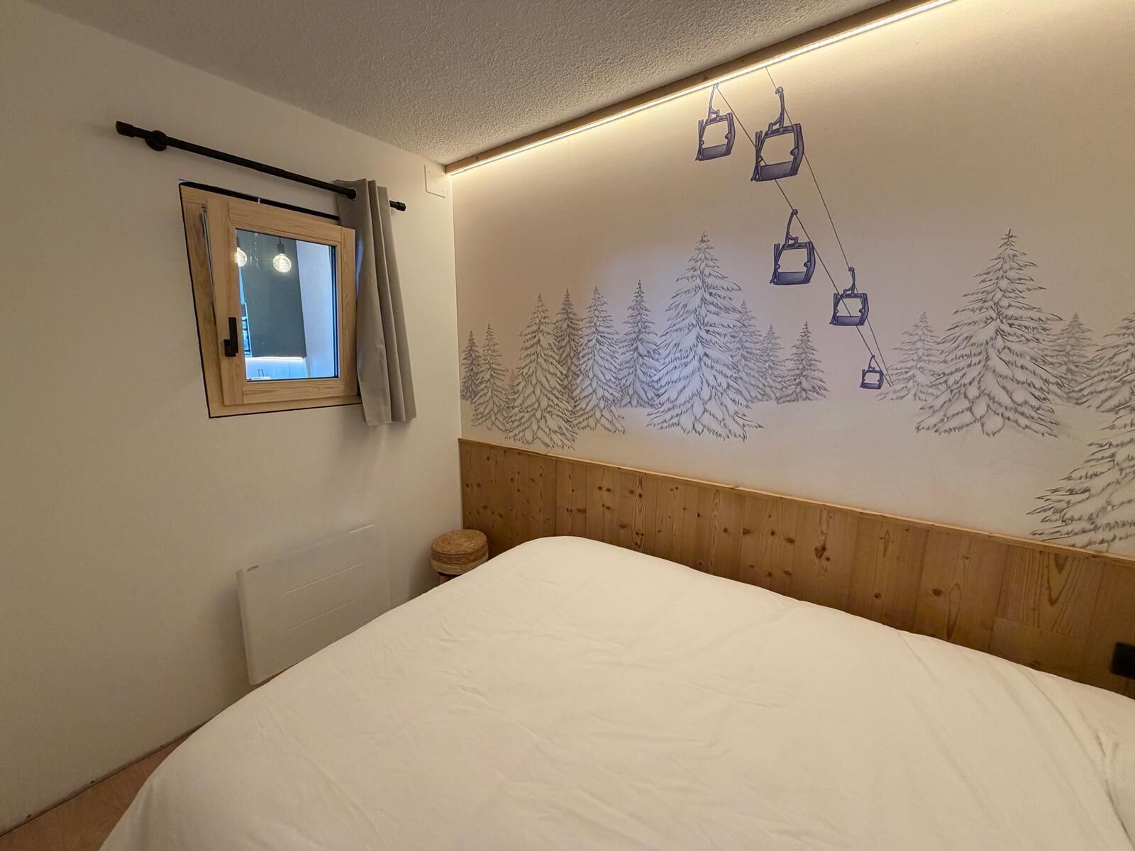 Ein Schlafzimmer mit Holz-Kopfteil, einem Fenster mit Vorhängen und einer Wandmalerei von Bäumen und Seilbahnen.
