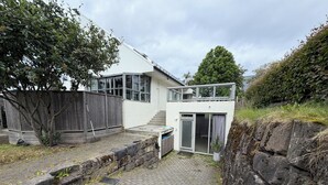 Una casa moderna de dos pisos con un patio empedrado, una valla de madera y un muro de contención de piedra.