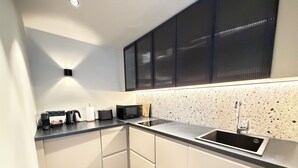 Una cocina moderna con encimera negra, armarios blancos, microondas integrado y pileta de acero inoxidable.