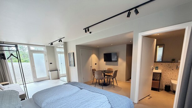 Habitación de hotel moderna con una cama grande, zona de comedor, televisión y baño.