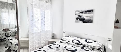 A modern bedroom with a large bed, a mirror, an air conditioning unit, and a view of the bathroom.