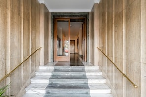 A marble staircase leading to a door with a glass panel, flanked by walls with vertical lines and a metal handrail. - Vatican Flat—2 Bedrooms, 2 En-suite Bathrooms, and a Balcony (Rome)