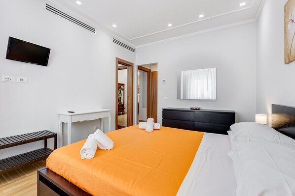 A modern hotel room with a large bed, a flat-screen TV, a desk, and a wardrobe. - Vatican Flat—2 Bedrooms, 2 En-suite Bathrooms, and a Balcony (Rome)