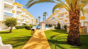Ein Hotel mit zentralem Pool, umgeben von gepflegten Rasenflächen und Palmen.