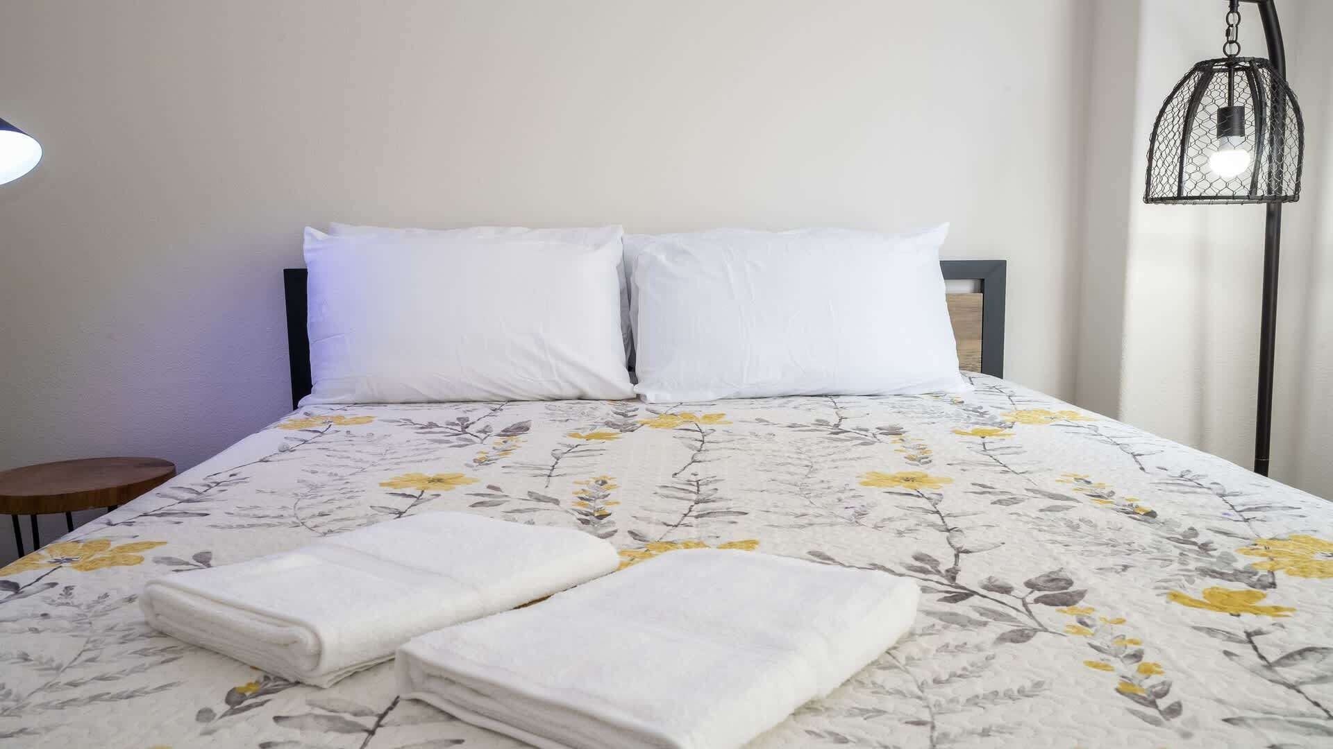 Una cama bien hecha con una colcha floral, dos almohadas y toallas dobladas.