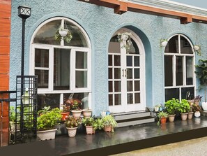 A building with three arched windows, a black metal gate, and multiple potted plants on the ground. - Classic Villa Barlow (Dehradun)