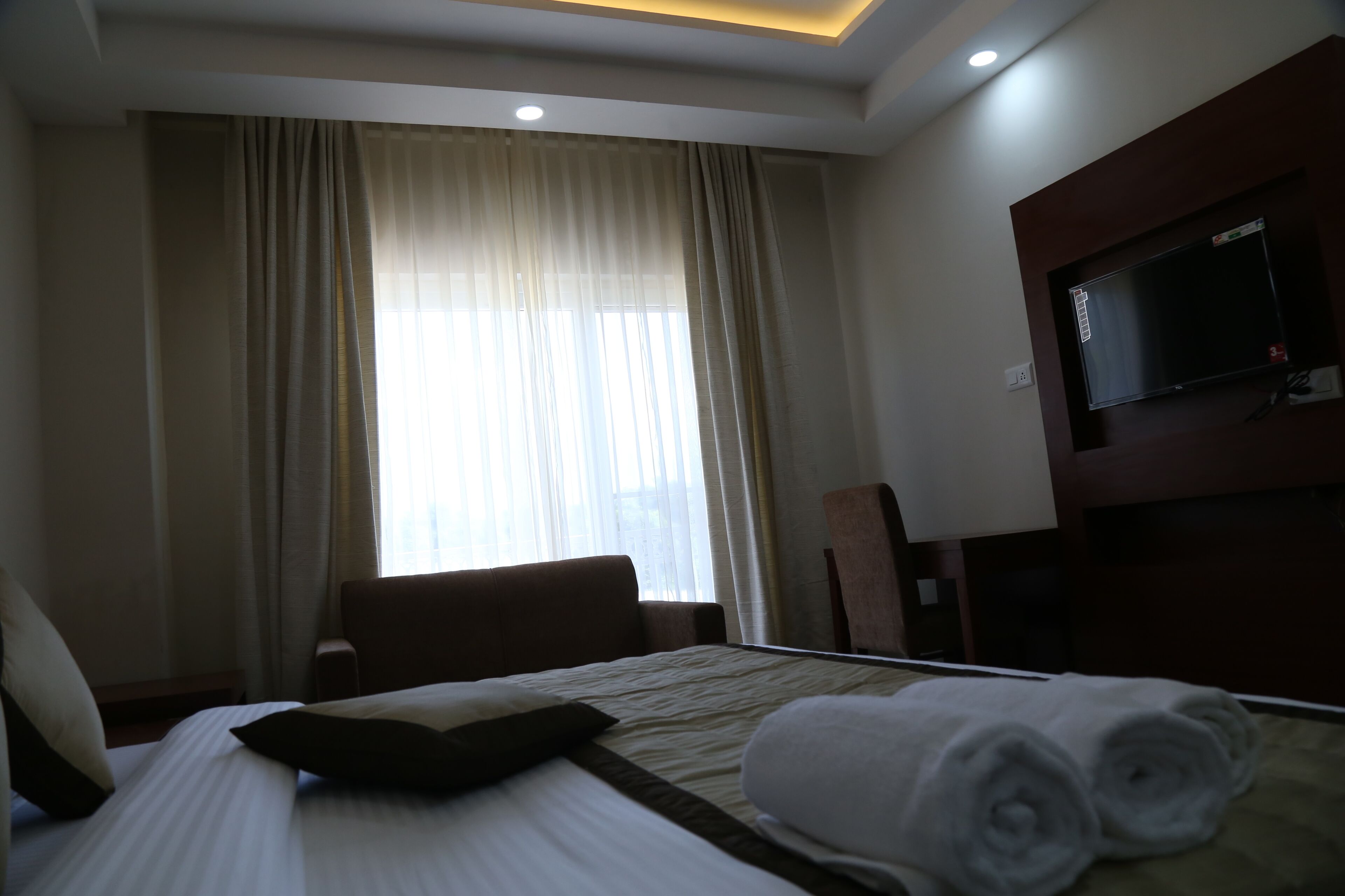 Una habitación de hotel con cama, una silla, un televisor y un ventanal con cortinas.