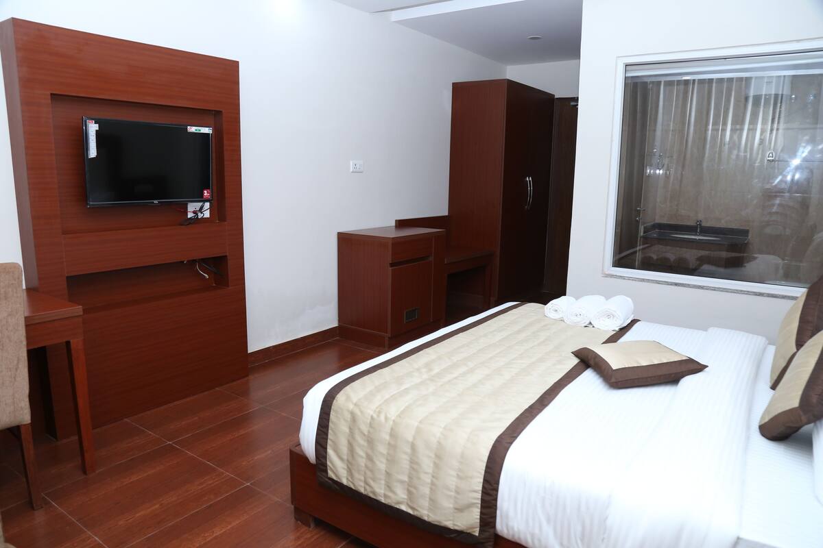 A hotel room with a bed, a TV mounted on the wall, a wardrobe, and a window with curtains.