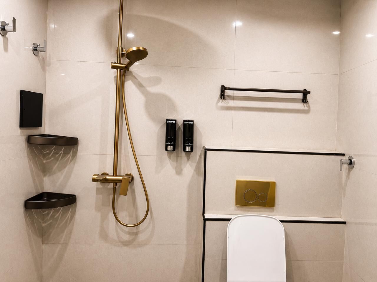 Ein modernes Badezimmer mit einer goldfarbenen Duschbrause, einer Toilette und zwei schwarzen Shampooflaschen.