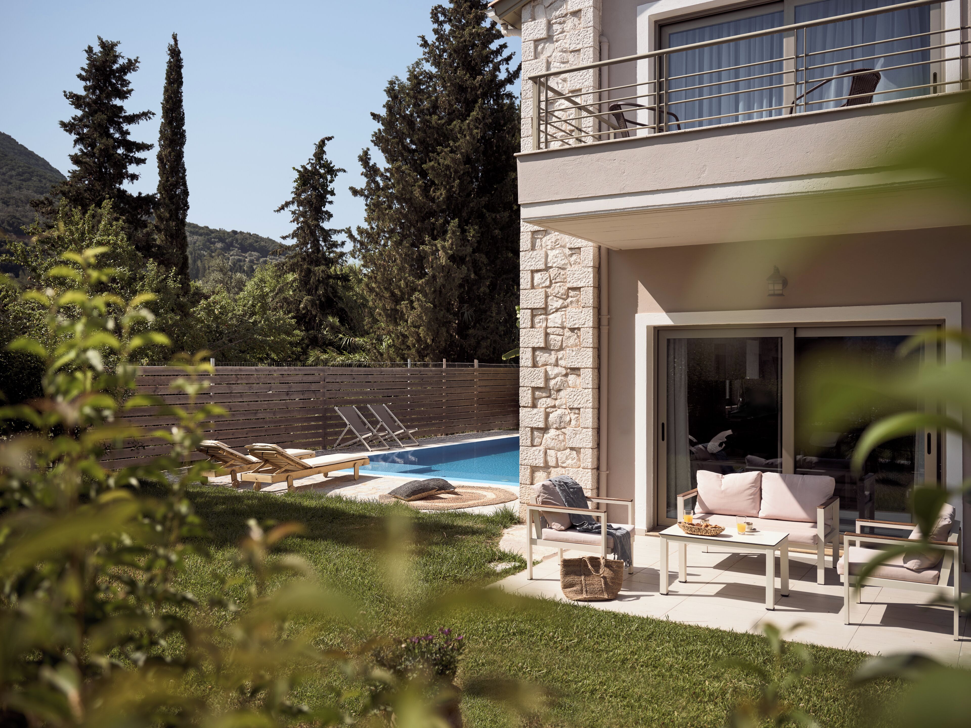 A modern two-story house with a pool, outdoor seating, and a stone wall.