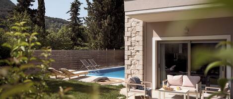 A modern two-story house with a pool, outdoor seating, and a stone wall.