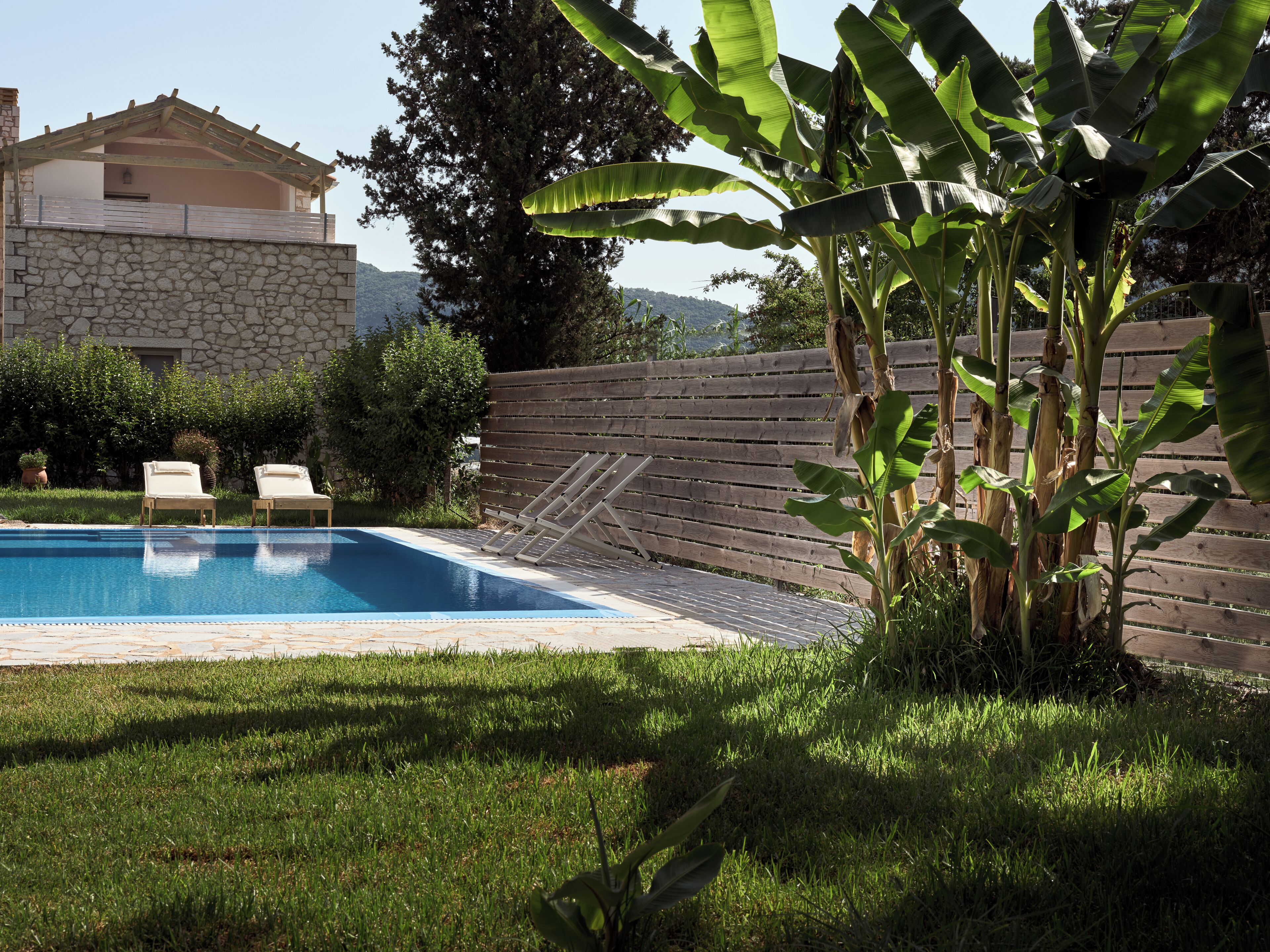 Une piscine avec deux chaises longues, un mur en pierre et une clôture en bois.